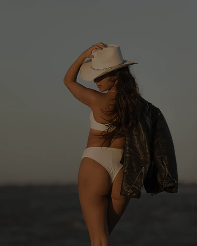 A wide-brimmed hat and leather jacket at dusk on the coast.